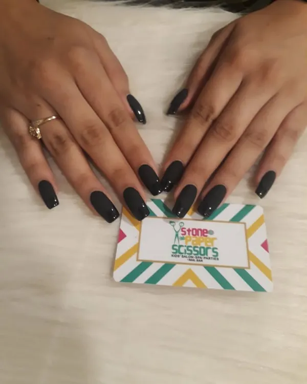 A full set of glossy black nails. This timeless and bold choice on medium-length coffin nails is always in style and adds a touch of sophistication to any look.