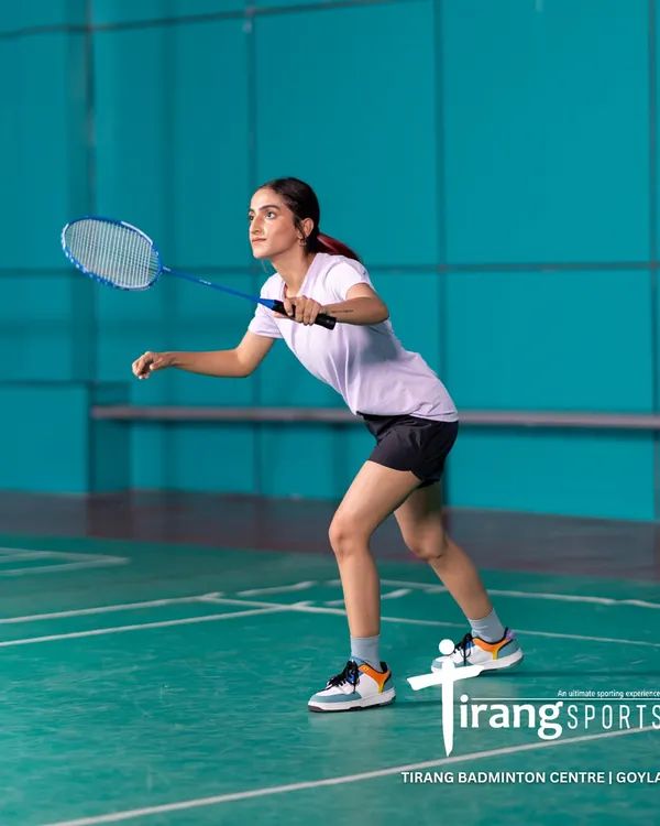 A player prepares for a backhand shot on our professional-grade court at the Tirang Badminton Centre in Goyla Vihar, Dwarka. The high-quality flooring and vibrant, non-glare walls create an ideal playing environment.