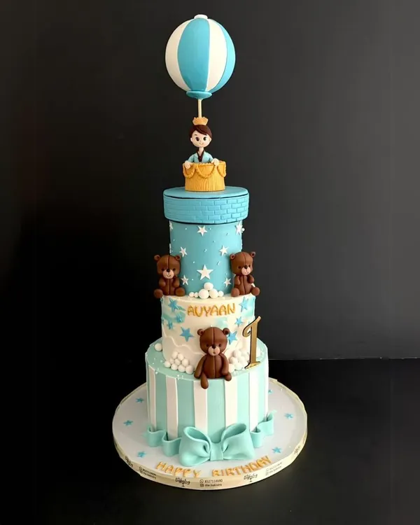 A grand celebration for a first birthday! This four-tiered cake for Avyaan features adorable teddy bears, a starry sky, and a little prince in a hot air balloon topper.