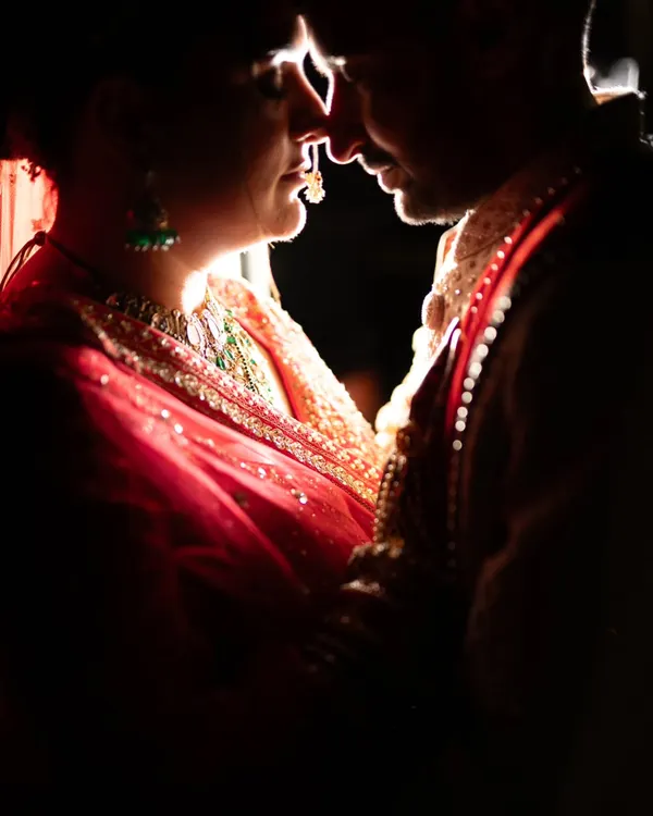 An intimate silhouette portrait of a couple in traditional attire. The dramatic rim lighting highlights their features and the intricate details of the bride's jewelry, creating a powerful and romantic image.