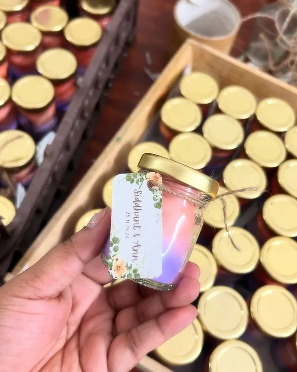 A close-up of a mini scented candle for a wedding. This one has a beautiful two-tone ombré effect and a custom floral label with the couple's names, Siddhant & Ann.