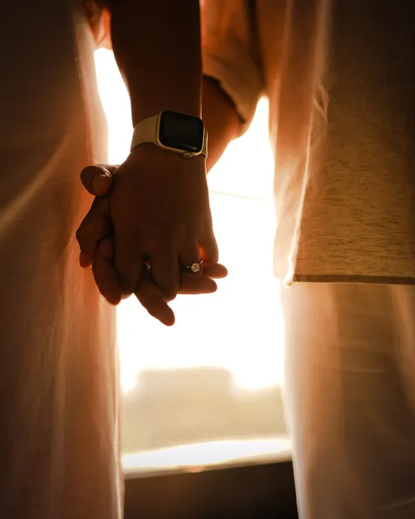 A close-up of the couple holding hands against the warm glow of the sun. The focus is on their intertwined fingers and the new engagement ring, symbolizing their connection.