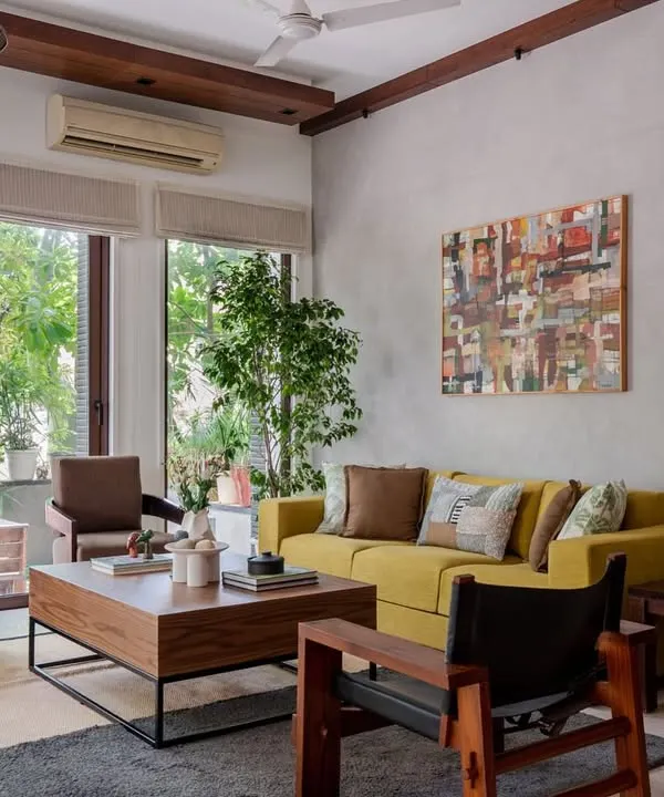 This living room seamlessly blends Tropical Modernism with Boho-Chic elegance. Large glass doors invite nature inside, while a lime-toned sofa and rich wooden finishes create a space filled with both calm and character.