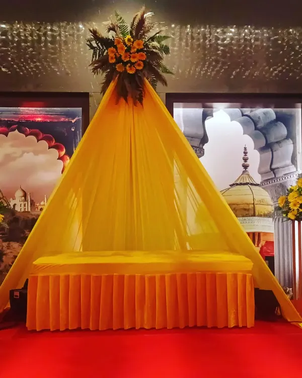 This is a special seating arrangement for a Haldi ceremony. I created a small, tent-like structure with yellow fabric and a floral top, providing a dedicated and decorated spot for the main rituals.