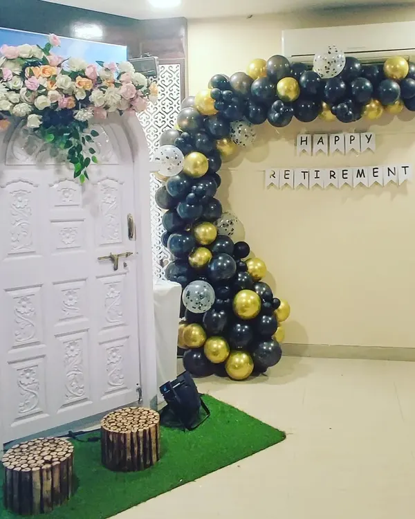 A modern take on retirement party decor. This organic balloon garland in a sophisticated black and gold palette adds a stylish touch to the celebration space, complemented by a decorative photo booth backdrop.