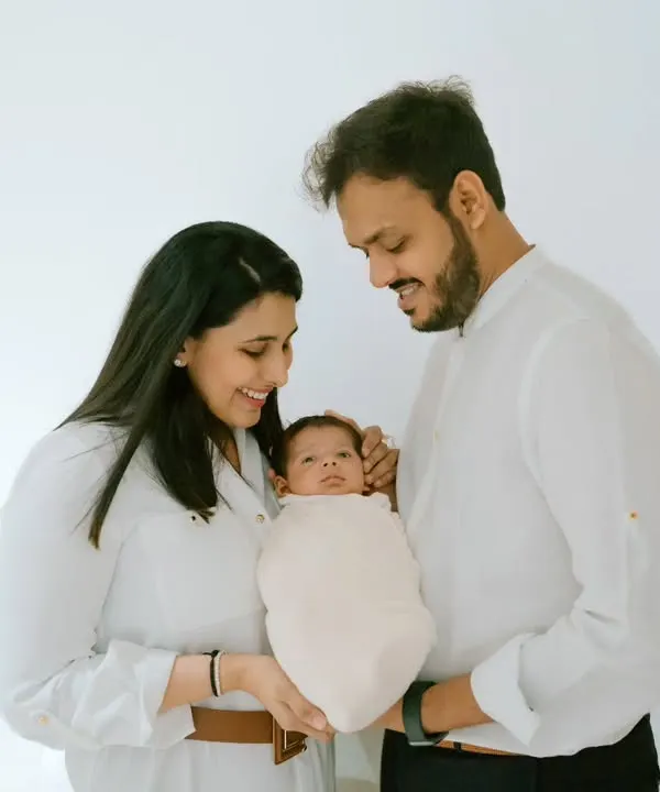 A classic all-white studio portrait beautifully highlights the connection between new parents and their precious newborn, wrapped snugly and held with so much love.