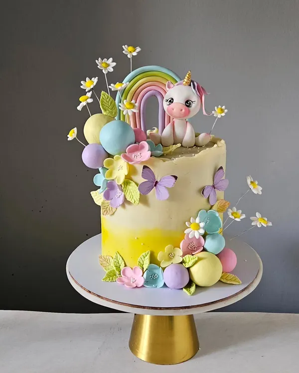 This magical unicorn cake is set in a pastel garden, complete with a rainbow, delicate sugar flowers, and fluttering butterflies. The unicorn figurine is hand-sculpted and sits atop a buttercream cake, making it a perfect fairytale centerpiece.