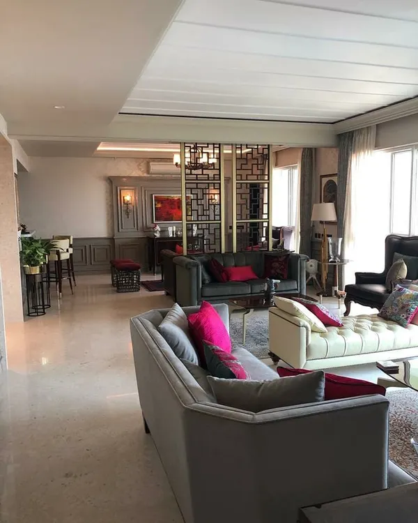 This living space is designed as an amalgamation of styles, blending classic comfort with contemporary details. The open-plan layout is defined by a geometric screen partition, creating distinct zones for lounging and a home bar while maintaining a cohesive flow.