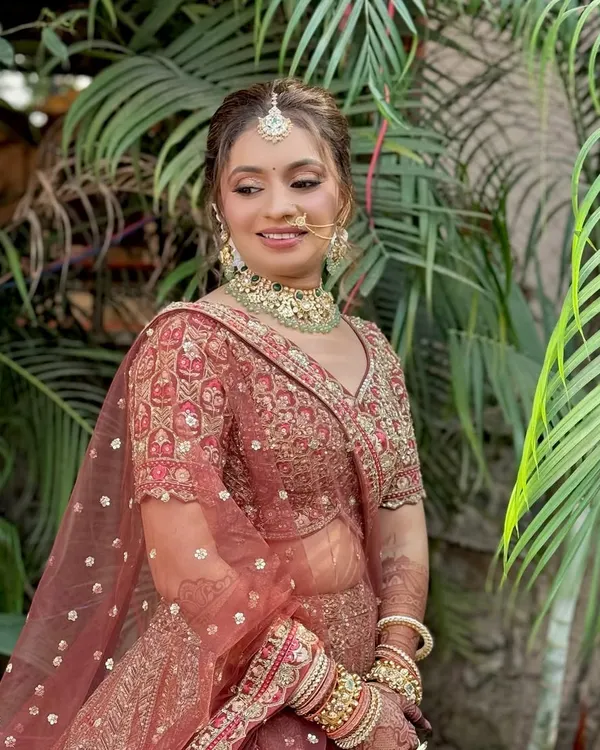 A beautiful bridal portrait showcasing a soft glam look with a focus on dewy skin and defined eyes, perfectly complementing her ornate red lehenga.