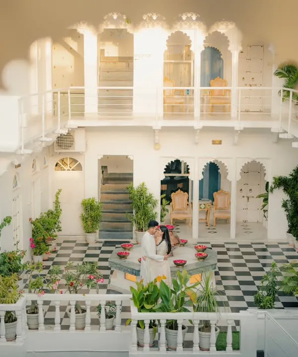 A wide-angle shot capturing the couple in a beautiful white courtyard in Udaipur. This image showcases the stunning architecture and creates a sense of privacy and grandeur.