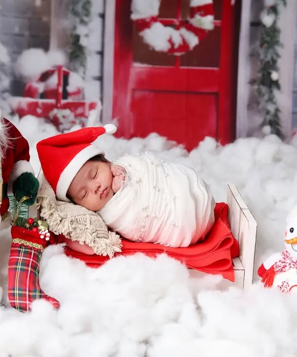 Your baby's first Christmas is a special milestone. Here, a newborn sleeps soundly in a sleigh, surrounded by a festive scene with Santa, a snowman, and a snowy backdrop.
