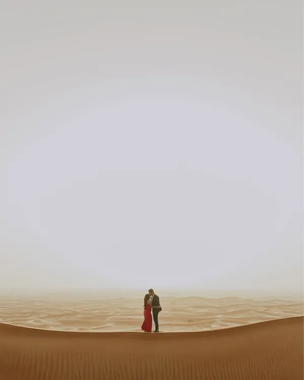 A minimalist yet powerful composition in the Dubai desert. The couple stands as a small, intimate focal point in the vast, empty expanse of sand and sky, emphasizing the idea that in a world of their own, only they matter.