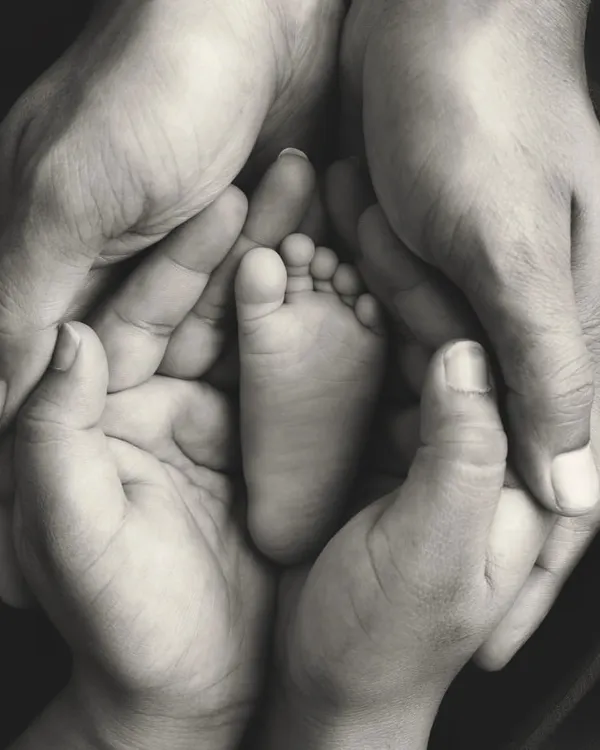 A baby's foot held safely in their parents' hands. This black and white image is a powerful and emotional symbol of family, protection, and love.