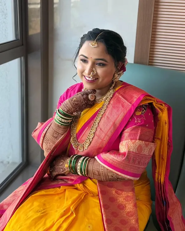 A beautiful Maharashtrian bride enjoying a quiet moment by the window. Her mandap look in a yellow and pink saree is designed to feel light on the skin and heavy on grace.
