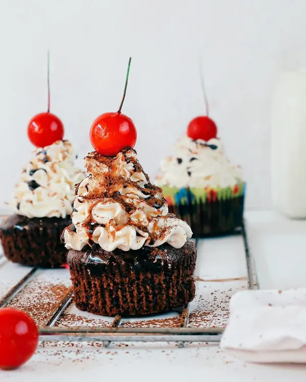 A trio of chocolate cupcakes, each topped with buttercream frosting and a bright red cherry. I used a clean, white background to make these treats the star, perfect for a bakery menu or a dessert blog.