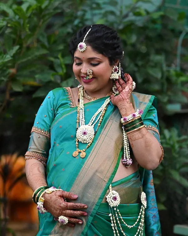 A beautiful portrait of a mom-to-be for her 'dohale jevan' or baby shower. She is glowing in a teal green saree, with soft makeup and delicate floral jewelry.