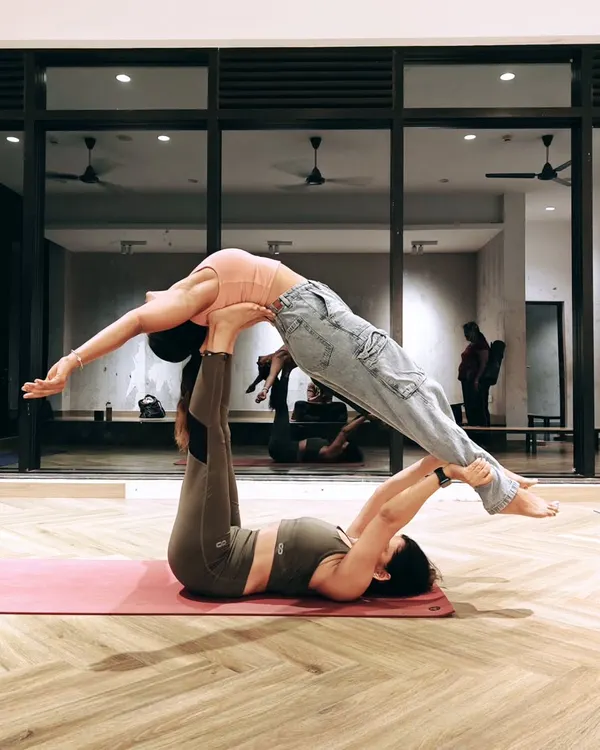 A classic Acro Yoga pose known as 'Front Bird'. The base lies on the ground providing a stable platform with their feet, while the flyer balances effortlessly, learning to trust and let go.