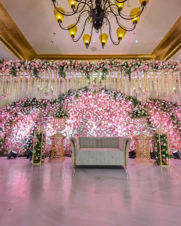 This reception stage is a masterpiece of floral art. A massive arching backdrop made entirely of pink and white flowers creates a breathtaking focal point, embodying pure romance and luxurious design.