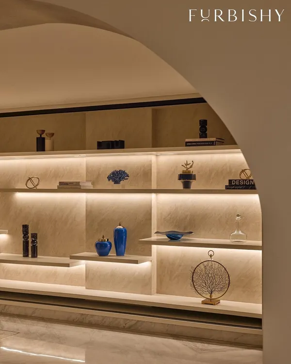 A foyer should have its own personality. For this entrance, I designed a custom backlit shelving unit to create a warm and dramatic welcome, using pops of indigo decor against sand-colored textured walls.