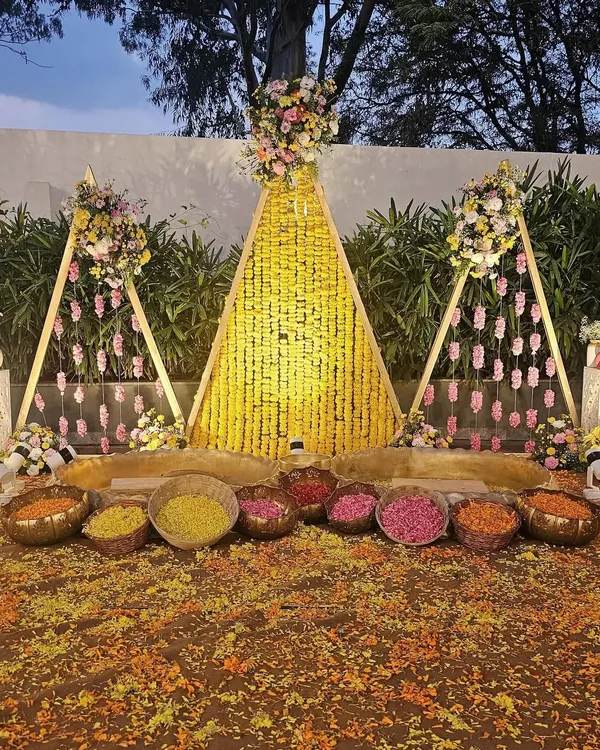 This is a beautiful and elaborate Haldi ceremony setup in an outdoor garden. I used triangular frames decorated with marigold garlands and rose hangings to create a stunning backdrop for the ritual.
