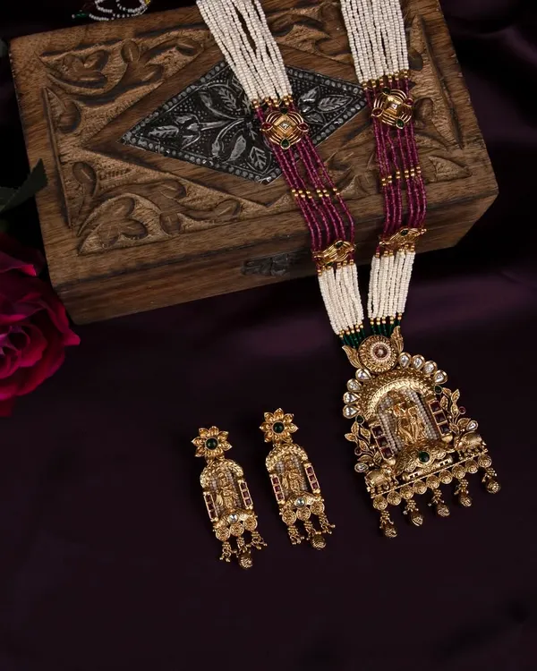 A complete traditional temple jewellery set, including a necklace and earrings, styled with a wooden box and a rose against a rich purple fabric for a luxurious feel.