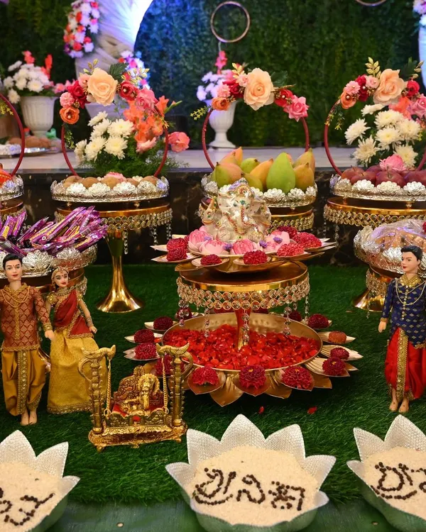 A complete naming ceremony setup with dolls representing the family, a central Ganesha pooja stand, and bowls with the baby's name written in grains.