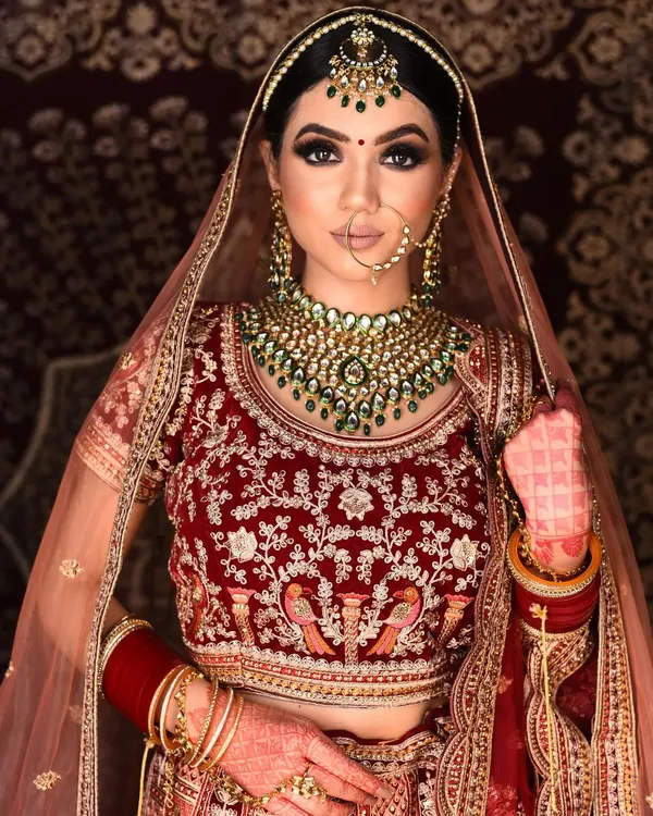A stunning example of a classic bridal look featuring a heavy Kundan necklace set with beautiful green stones. This set is perfect for pairing with traditional red or maroon lehengas.