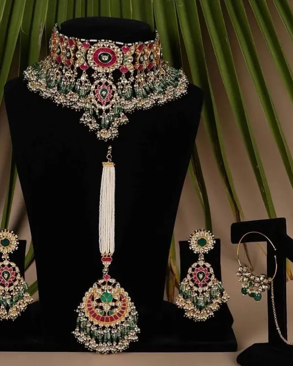 A magnificent bridal choker set with matching earrings, maang tikka, and nath. The combination of red, green, and white stones makes it a versatile piece that can be paired with many different lehengas.