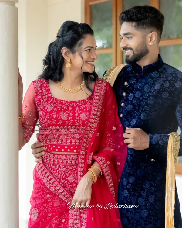 A picture-perfect couple at their engagement. The bride-to-be has a natural, glowing makeup look that enhances her features, paired with a beautiful red lehenga.