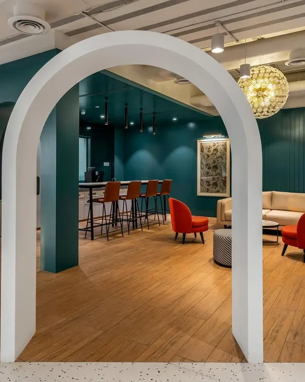 A breakout space in the Asian Paints office, framed by a clean white arch. The design uses bold colors, like the deep teal wall and red chairs, to create an inviting and energetic atmosphere for informal meetings and breaks.