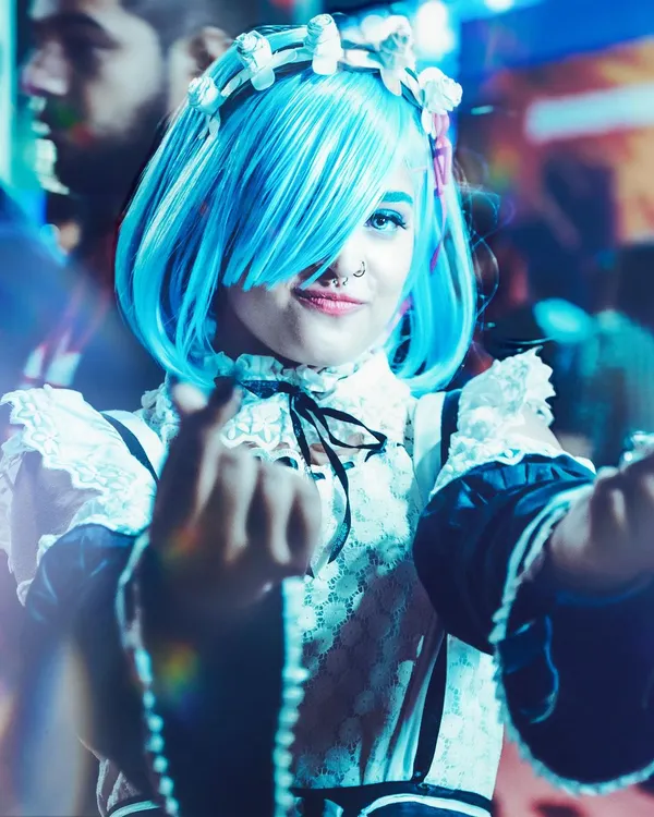 A vibrant, close-up shot of a cosplayer as REM from Re:Zero, captured at Comic Con Delhi. We use creative lighting and angles to match the anime aesthetic, highlighting the bright blue wig and character's signature pose.