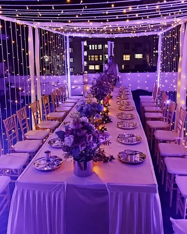 This is another view of the enchanting rooftop dinner setup, showcasing how we use ambient lighting to completely change the mood. Here, purple lights complement the fairy light canopy for a sophisticated and memorable evening.