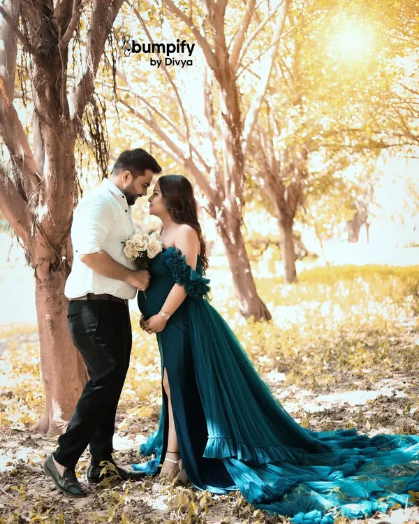 A romantic outdoor maternity portrait of a couple, bathed in the soft golden hour light. The way her teal gown flows in the gentle breeze adds a touch of fairytale magic to their special moment.