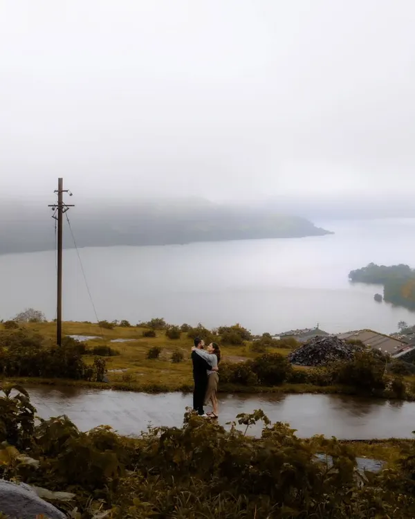 An embrace against a vast, misty lake and rolling hills. This epic wide shot captures the scale of nature, making the couple's intimate moment feel even more significant and romantic.