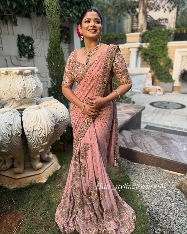 A full-length view of a client in a beautifully draped pink saree, paired with an elegant updo. This shows how I coordinate the hairstyle and saree draping for a cohesive look.