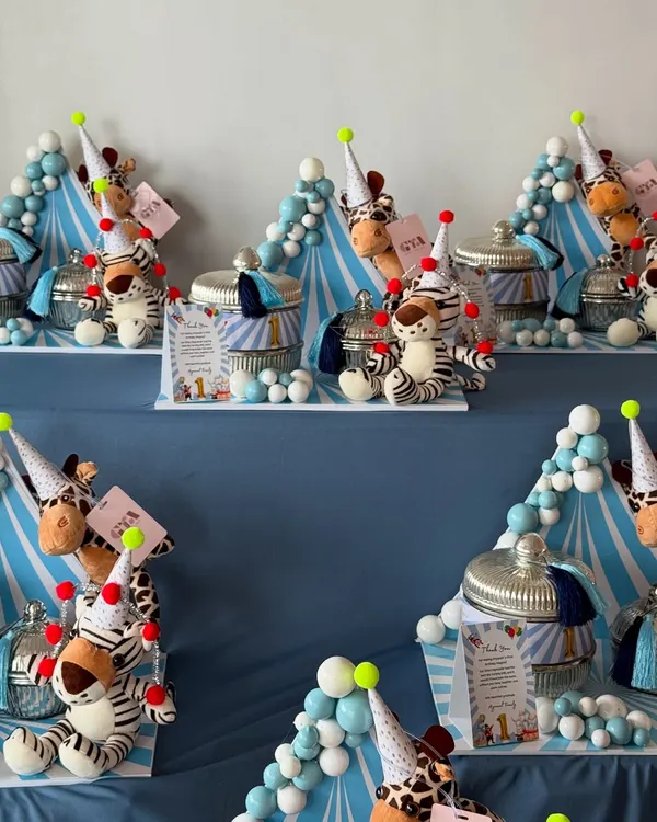 Step right up! A display of jungle-circus themed return favors for a first birthday, featuring plush animals in party hats and decorative jars.