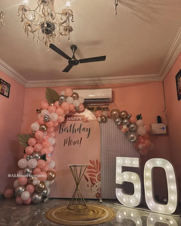 A beautiful and elegant setup for a 50th birthday celebration for a mom. The soft pink backdrop, combined with rose gold and silver balloons and large marquee numbers, creates a warm and celebratory feel.