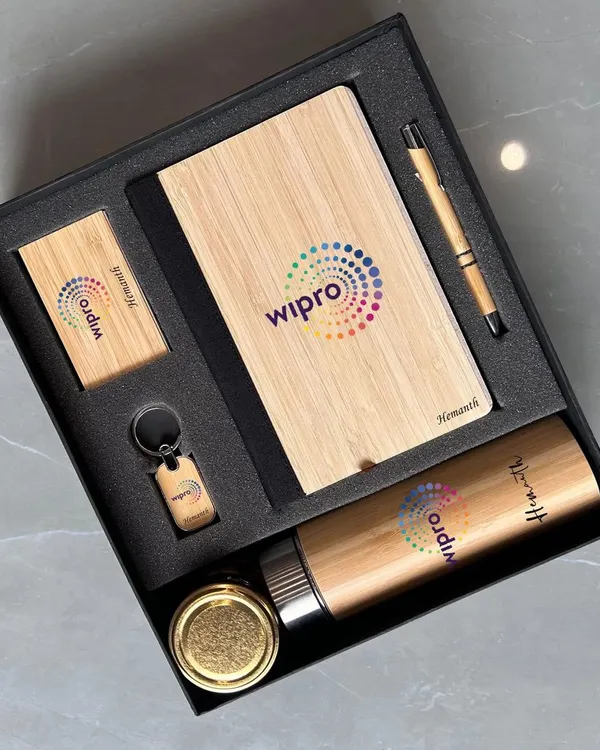 This eco-friendly corporate gift set for Wipro features items made with bamboo accents. The set includes a bamboo notebook, pen, bottle, keychain, and card holder, all branded with the company logo for a sustainable and stylish gift.