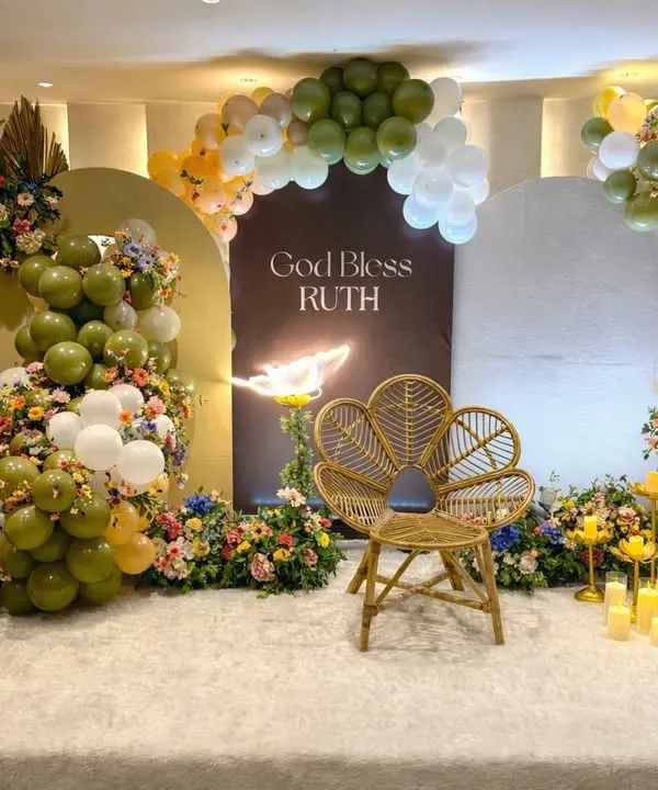 A full view of this sophisticated blessing ceremony stage. The design balances modern arched backdrops and balloon decor with timeless elements like fresh flowers, a natural wicker chair, and an array of flameless candles for a warm glow.