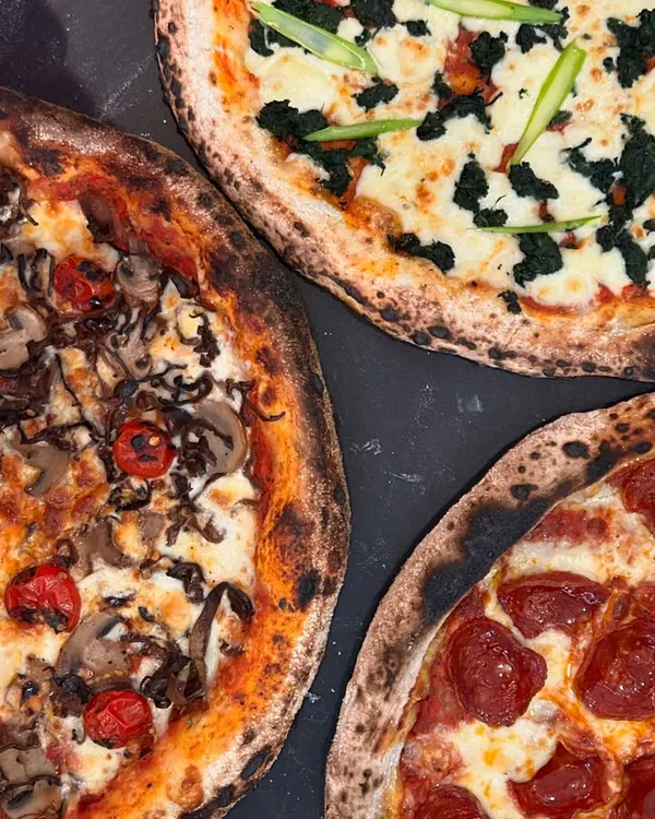 A trio of our artisanal pizzas, showcasing the variety of fresh toppings we use, from pepperoni and mushroom to spinach and asparagus.