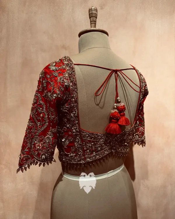 A Muhurtham masterpiece for Bhavya. This rich red raw silk blouse features a breathtaking wedding procession concept on the back, brought to life by masterful hands.