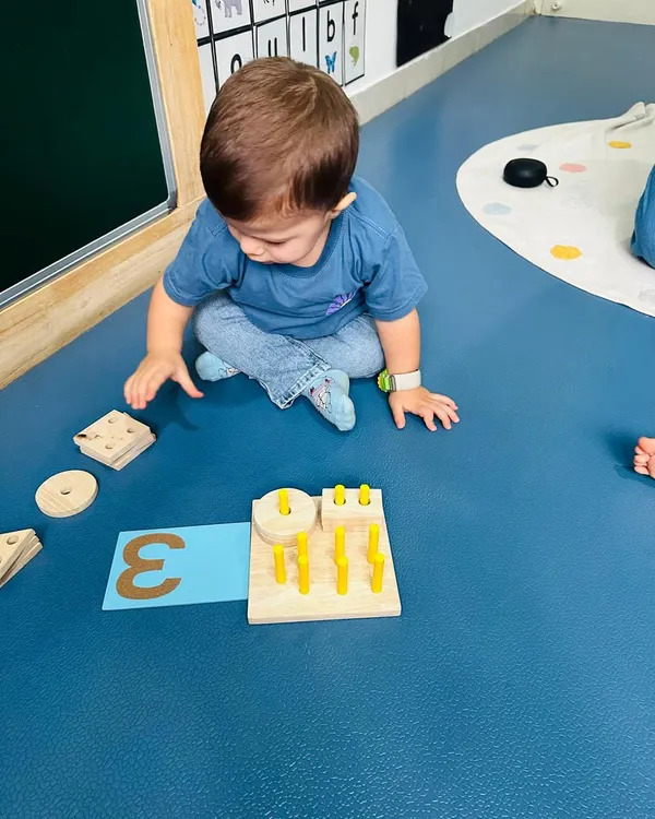 A toddler explores shapes and numbers with a wooden puzzle. My training emphasizes using natural, tactile materials to introduce foundational concepts like numeracy and geometry.