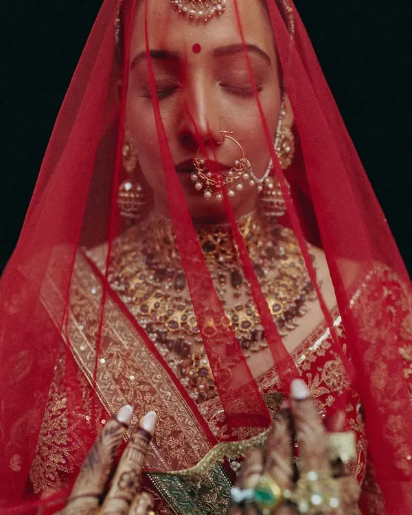 A powerful, artistic close-up of the bride Rakhi, her face veiled in red, capturing a moment of serene contemplation.