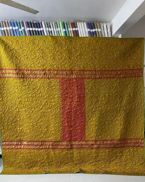 A full view of a reversible memory quilt made from a client's precious saree. We carefully incorporated the saree's original borders into the design, finished with a dense, floral longarm quilting pattern for durability and texture.