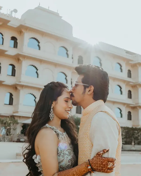 A tender forehead kiss in the warm sunlight, with the beautiful architecture of a Udaipur palace hotel providing a stunning, regal backdrop.