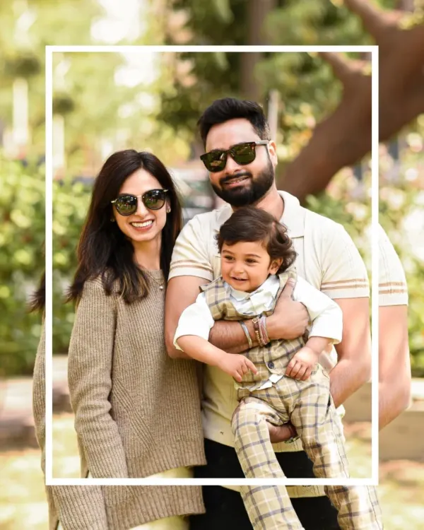A stylish family of three poses for a portrait during their outdoor session in a park. The natural sunlight and greenery create a warm and vibrant backdrop.