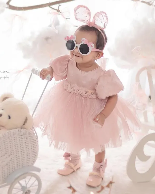A little fashionista celebrating her first birthday. The fun sunglasses, pink tulle dress, and dreamy cloud background come together for a stylish and memorable milestone portrait.