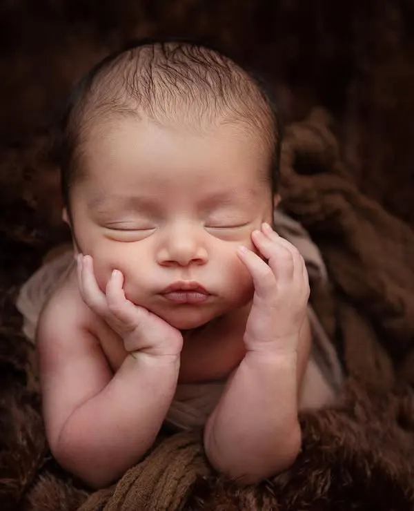 This classic 'chin on hands' pose is a favorite for newborn photography. I achieve this pose safely and patiently while the baby is in a deep sleep, resting on a soft, furry blanket.