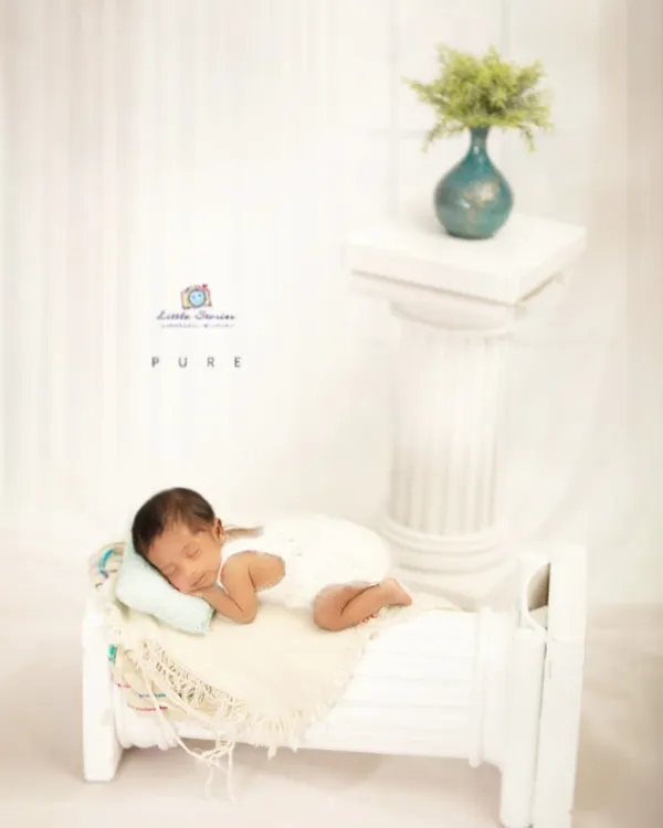 This all-white setup creates a clean, serene, and timeless image. The miniature bed prop allows for a natural sleeping pose while adding a touch of classic elegance to the newborn portrait.