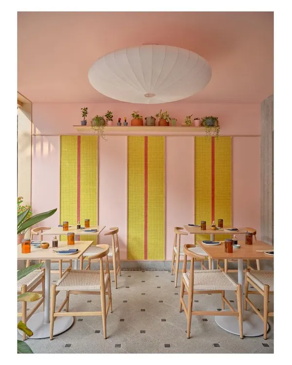 The alfresco dining area at Lucky Chan combines a playful pink wall with bold yellow and red tile panels. The design uses color and pattern to create a cheerful and highly photogenic restaurant interior.